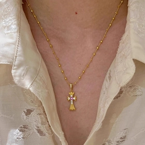 Detailansicht einer goldenen Kreuzkette mit rosa Edelstein und kleinen weißen Diamanten darauf