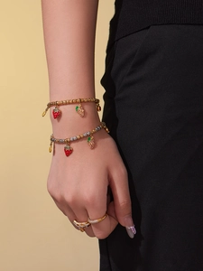 Close-up of gold beaded bracelets with strawberry and grape enamel charms and rings