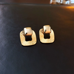 Macro detail of gold-plated geometric square earrings with textured metallic finish