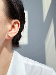 Close-up of a minimalist gold bar earring worn by a model in natural window light