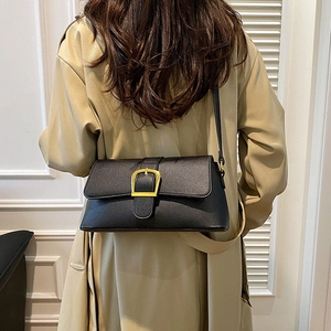 Detail of black pebbled leather texture and gold buckle on stylish shoulder baguette bag