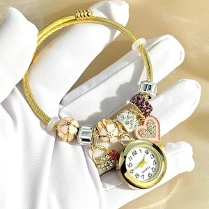 Golden charm bracelet watch featuring pink flower pendants and crystal beads on a textured band