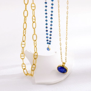 Macro shot of gold pig nose chain link with navy blue beaded necklace and gem pendant