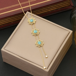 Gold double-chain necklace with turquoise flower pendants on beige jewelry box