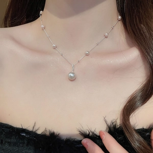 Close-up of elegant pearl pendant necklace on model's collarbone with black feather detail