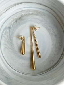 Detailed view of three gold teardrop earrings in various sizes on marble textured plate