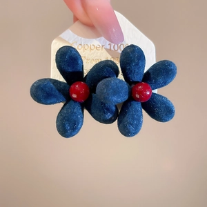 Macro shot of dark blue flocked flower earrings with red centers and velvet texture