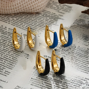 Detailed shot of U-shaped enamel hoop earrings in white, blue and black over vintage paper
