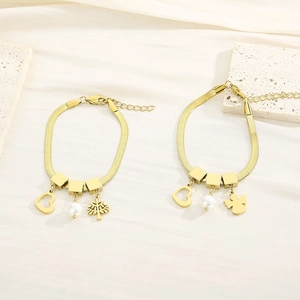 Detail of golden snake chain bracelets with heart, pearl, and angel charms on stone