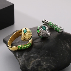 Close-up of gold and silver snake rings with green enamel and emerald-colored gemstones