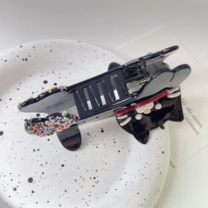 Close-up of black cat hair claw clip with colorful sequins on a white ceramic plate