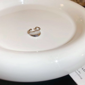 Close-up of irregular wave-shaped silver ear cuff on a white ceramic plate