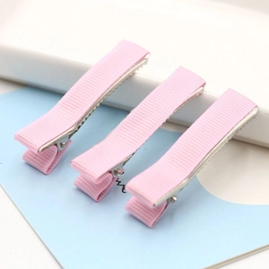 Close-up of three pink ribbed fabric-wrapped metal alligator hair clips on a soft background