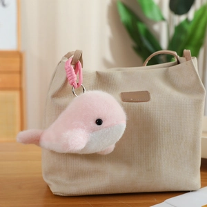 Detail of pink whale plush keychain with metal clasp hanging on a canvas bag