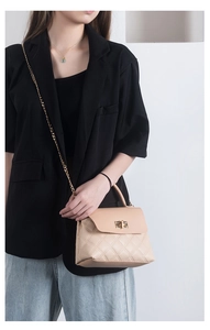 Close-up of beige quilted PU leather chain bag with square metal lock worn by a model
