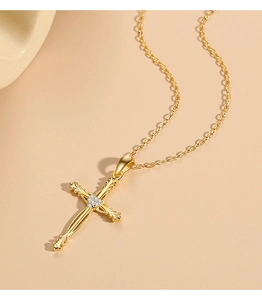 Detail of gold cross pendant with intricate engraving and heart-shaped zircon inlay