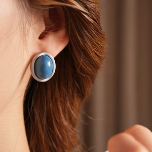 Close-up of minimalist silver oval earrings with blue resin center on model's ear