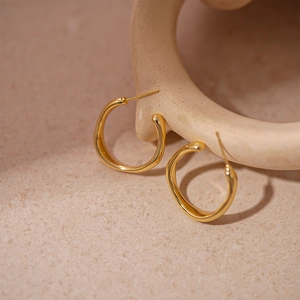 Détail de boucles d'oreilles créoles dorées géométriques sur fond beige texturé