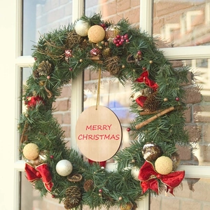 Christmas wreath with pine cones and red bows hanging on a door with a merry christmas sign
