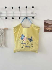 Detail of yellow tote bag with blue butterfly embroidery and blue checkered handle