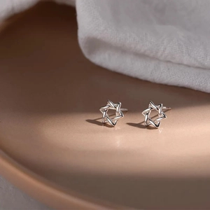 Macro shot of silver hollow star studs on ceramic tray with elegant fabric background