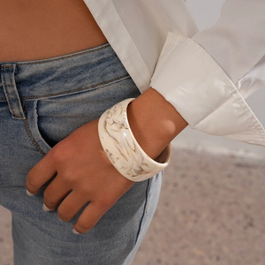 Close-up of wide resin bangle with marble pattern worn with a white shirt and denim