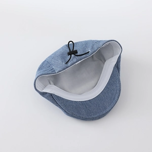 Detail view of denim newsboy cap showing blue twill fabric and inner lining with drawstring