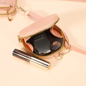 Pink round leather coin purse with gold zipper holding keys and lipstick inside