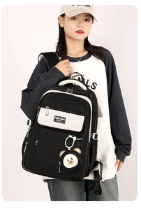 Macro detail of black and beige high-capacity school backpack with cute bear pendant