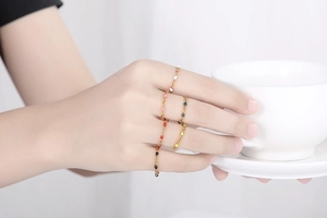 Dettaglio di un anello a catena d'oro con perline di smalto colorato su una mano con tazza