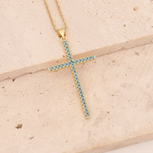 Close-up of golden cross pendant with turquoise stones on marble background