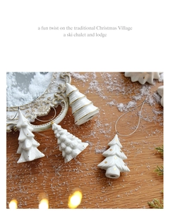 Three white ceramic Christmas tree ornaments with gold dots on rustic wooden background