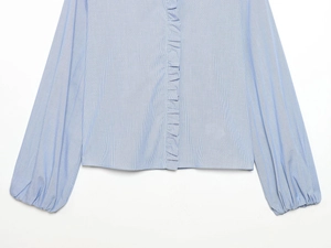 Detail of light blue striped poplin shirt featuring ruffle trim and elastic lantern cuffs