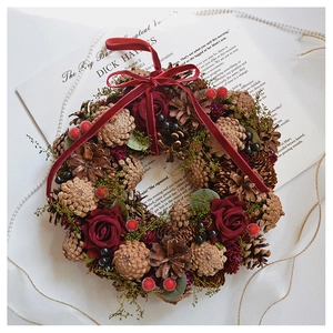 Detail of vintage Christmas wreath with red roses, pine cones, and a velvet bow