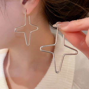 Close-up of large silver star-shaped hoop earrings worn by a model in casual knitwear