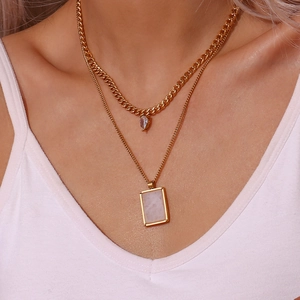 Close-up of gold layered necklace featuring a thick Cuban chain and crystal pendants