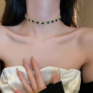 Gros plan du collier choker doré avec pierres vert émeraude et strass scintillants