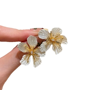 Elegant white floral earrings with golden pistils and crystals in hand-held display