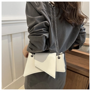 Close-up of asymmetrical white leather shoulder bag with fine silver chain strap on model