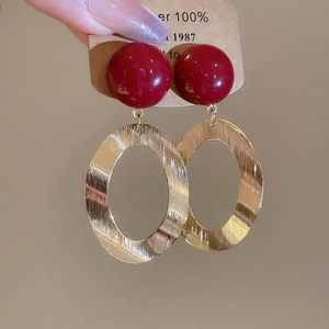 Detail view of red resin bead and brushed gold oval metal earrings on a display card