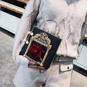 Detailed shot of black baroque box bag featuring a red rose and elegant pearl pendant