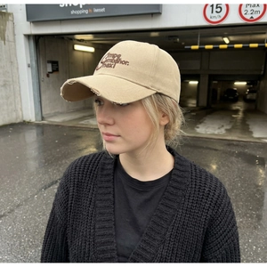 Detail of beige vintage washed baseball cap featuring distressed brim and brown embroidery