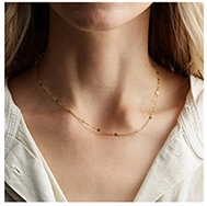 Gros plan d'un collier doré minimaliste avec pampilles porté par un mannequin au clavicule