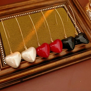 Three pairs of heart pendant drop earrings in white, red and black on a vintage wood display