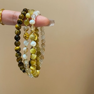 Détail de bracelets en perles avec œil de tigre, cristal blanc et pendentifs dorés