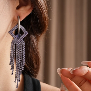 Macro shot of purple rhinestone geometric drop earrings with long tassel fringe on ear