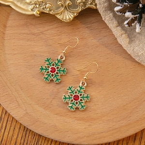 Detail shot of green snowflake earrings with a red rhinestone on a rustic wooden base