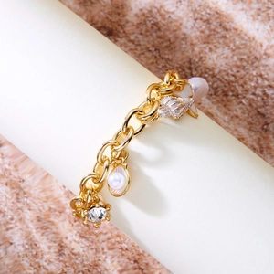 Detail of gold ocean theme bracelet with pearls, shells, and starfish on sand texture