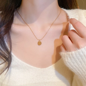 Gros plan d'un collier pendentif ovale doré porté sur un pull en maille blanc