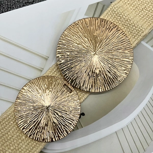 Detail of beige woven belt featuring gold-tone circular metal buckles with radial texture